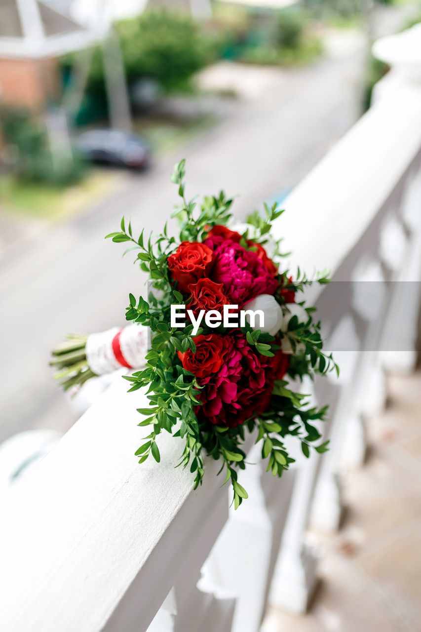 Bouquet of red roses and red and white peonies on a background of white stone railing