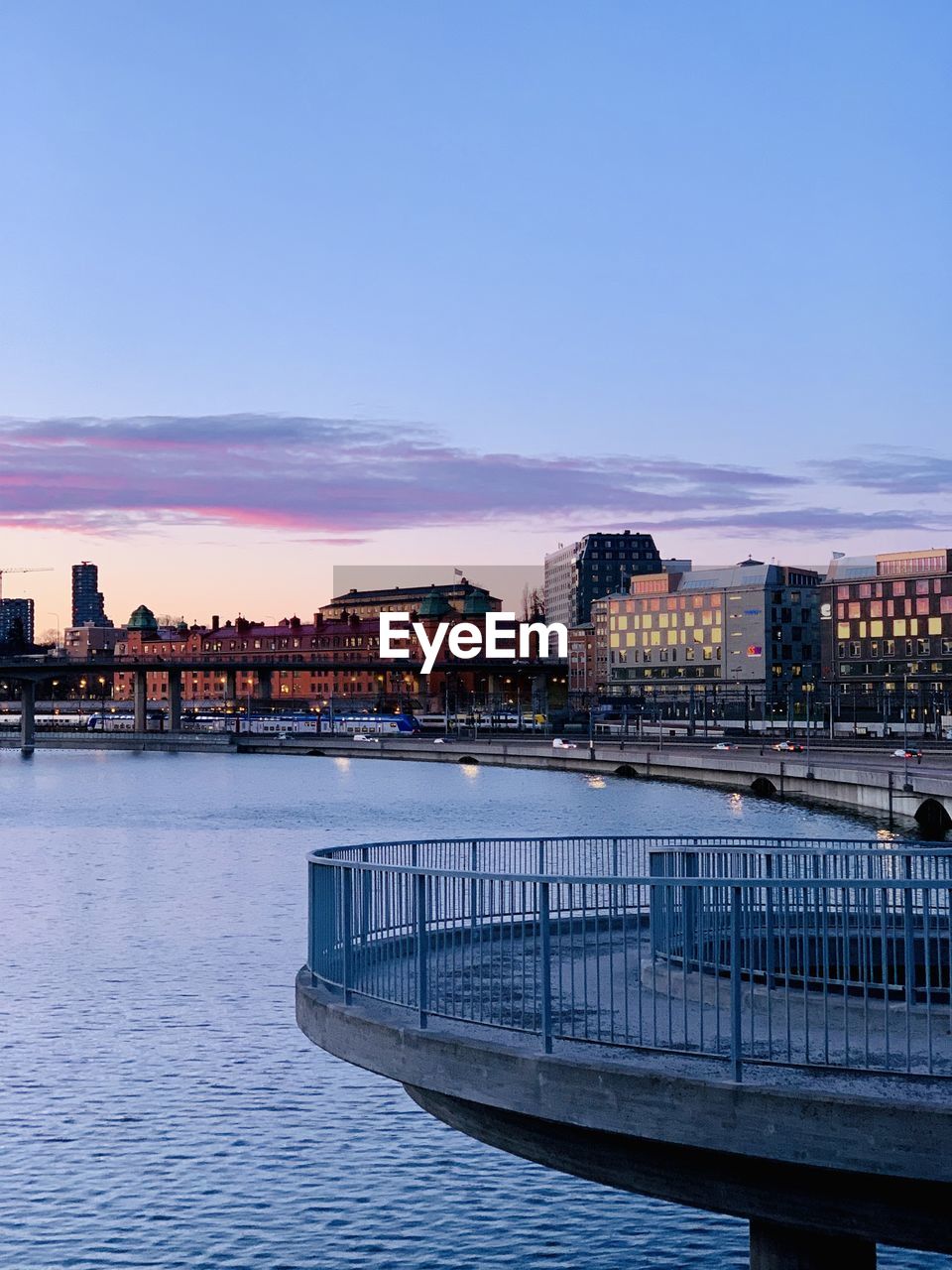 Bridge over water by buildings against sky at dusk