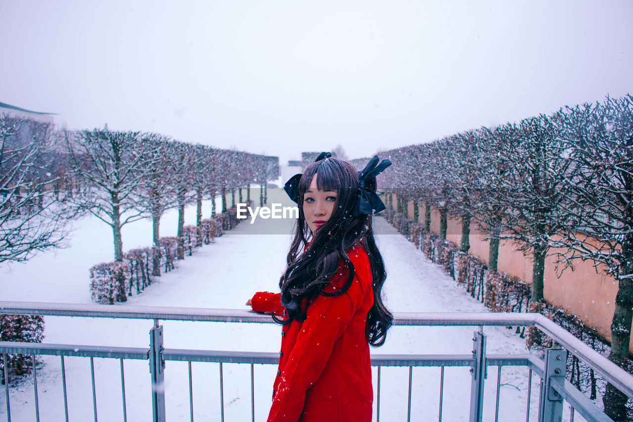 Portrait of young woman standing on snow covered railing