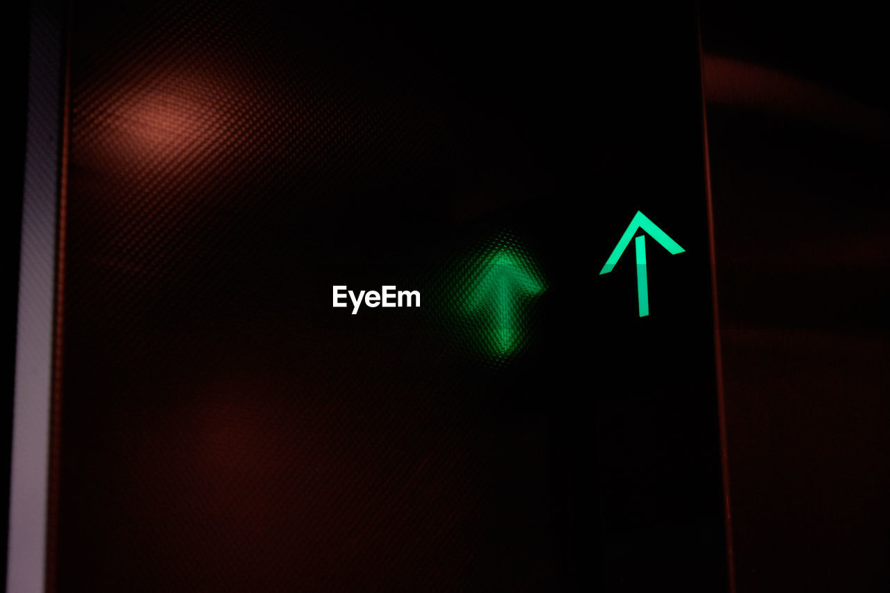 Low angle view of illuminated green arrow with reflection in dark elevator