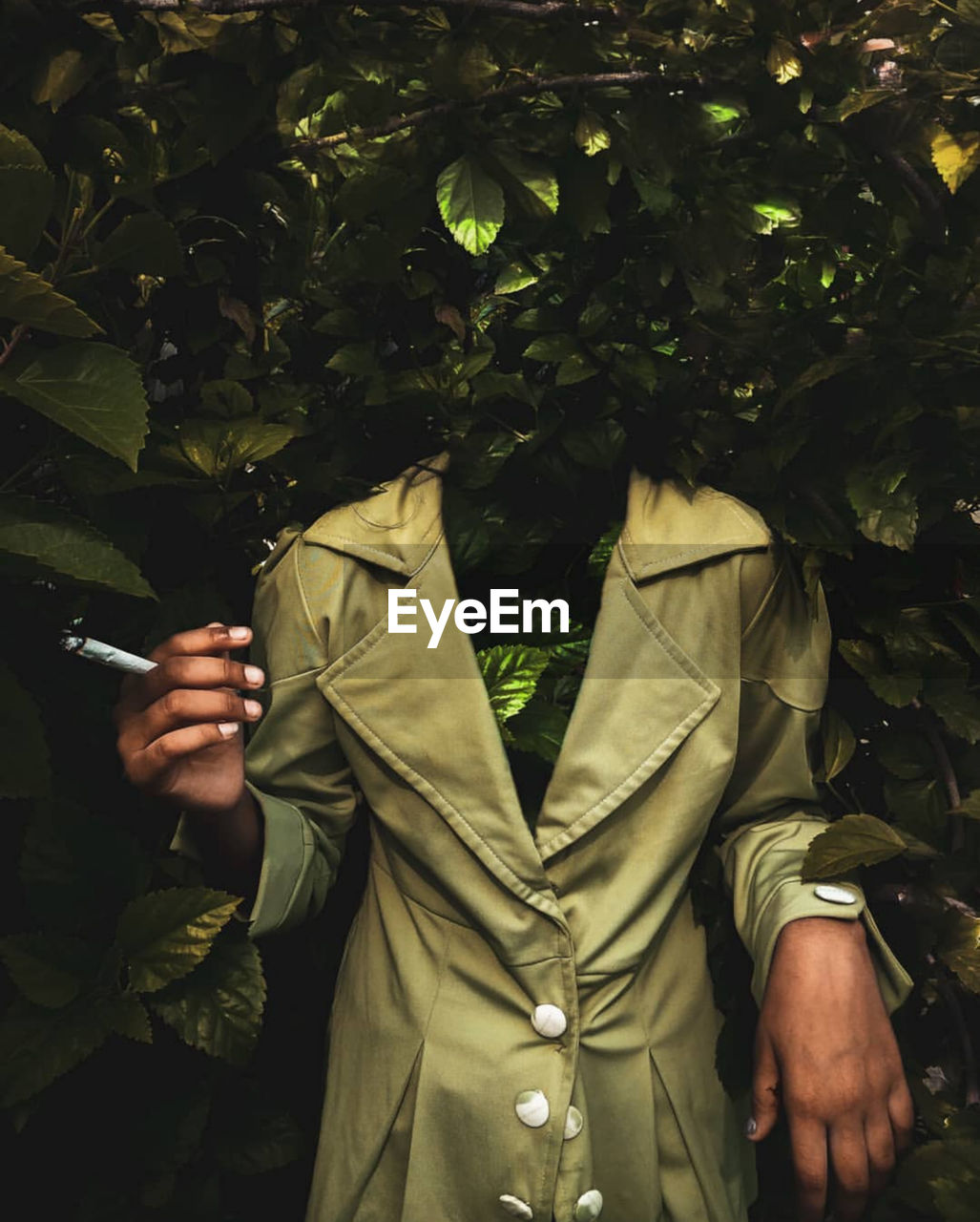 MIDSECTION OF MAN HOLDING MOBILE PHONE WHILE STANDING ON PLANT