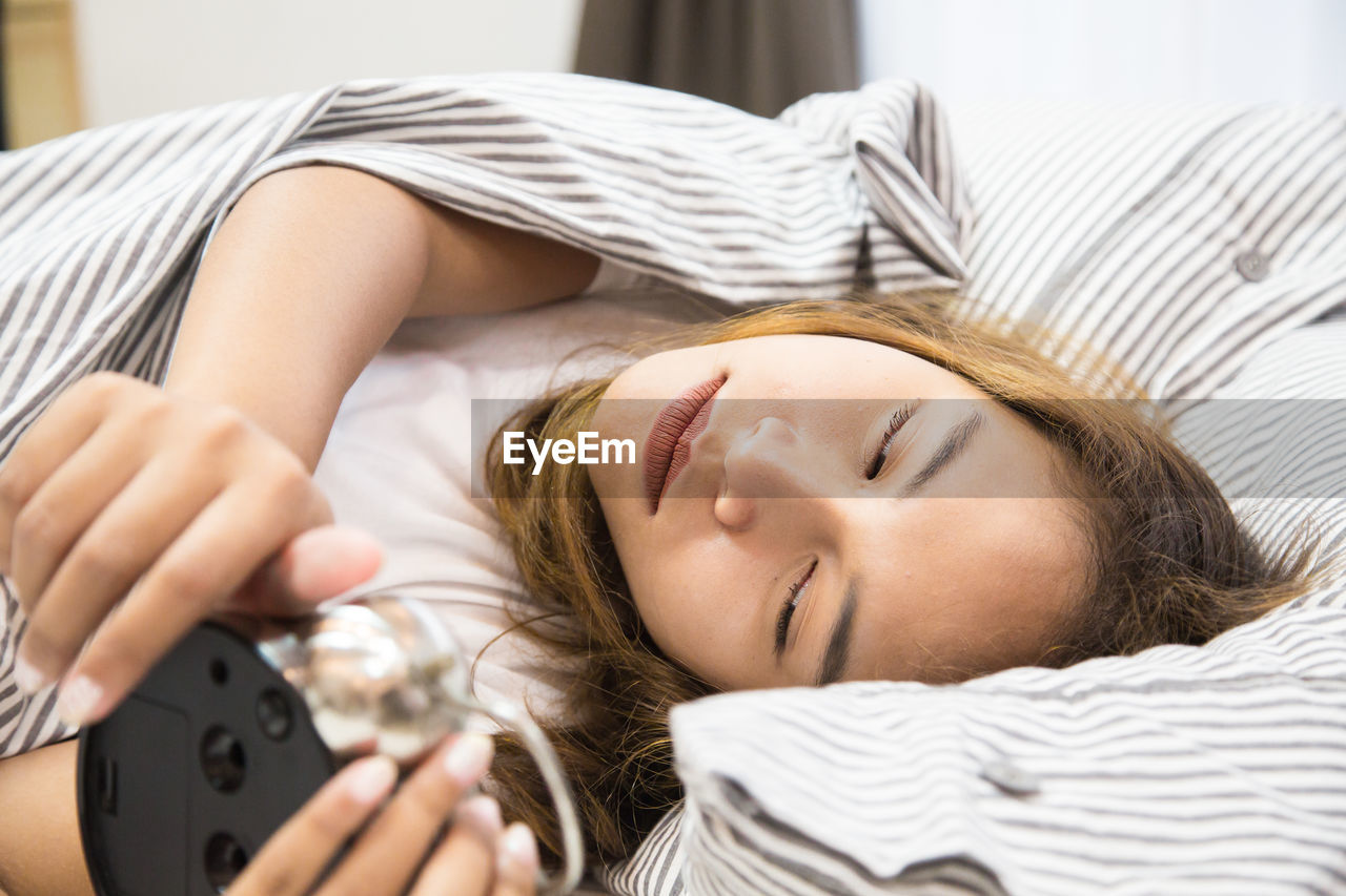 Woman holding alarm clock while lying down on bed