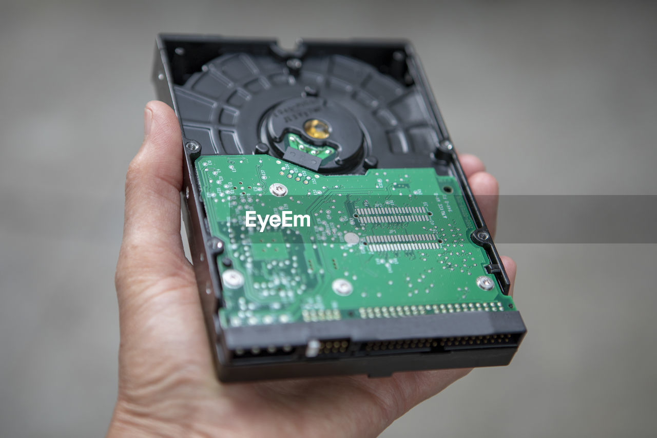 Close-up of person hand holding computer circuit board against gray background