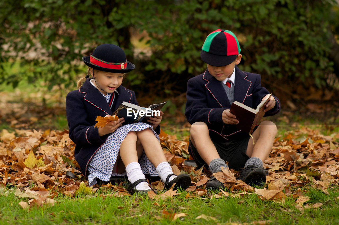 Full length of boy and girl reading books while sitting on grass