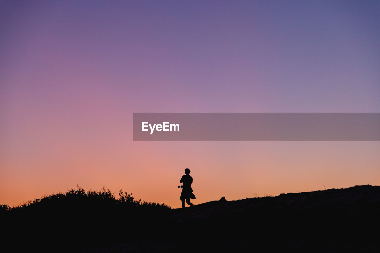 Silhouette of a woman standing against a clear sky during sunset