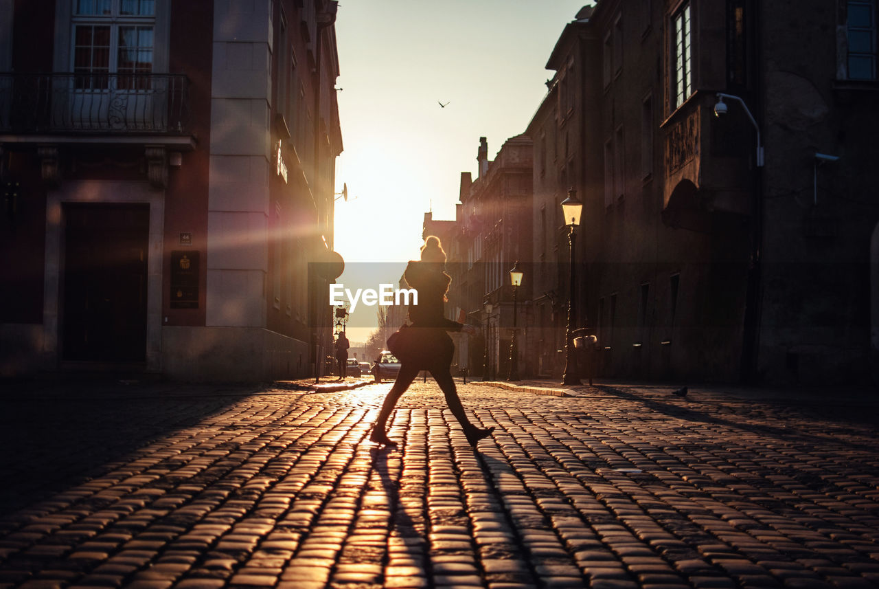 MAN WALKING ON STREET AMIDST BUILDINGS AGAINST SKY
