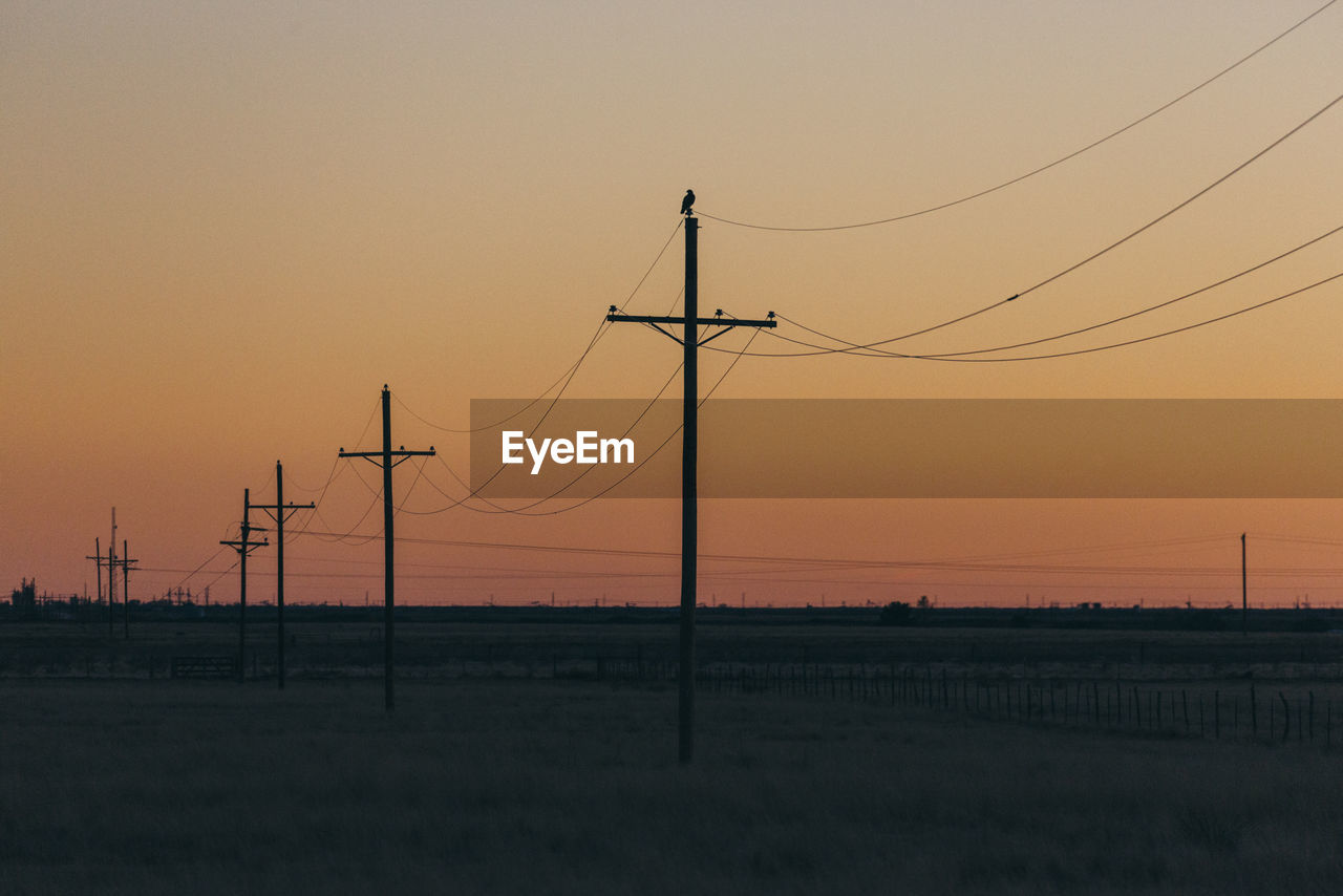 Low angle view of electricity pylons against sky during sunset