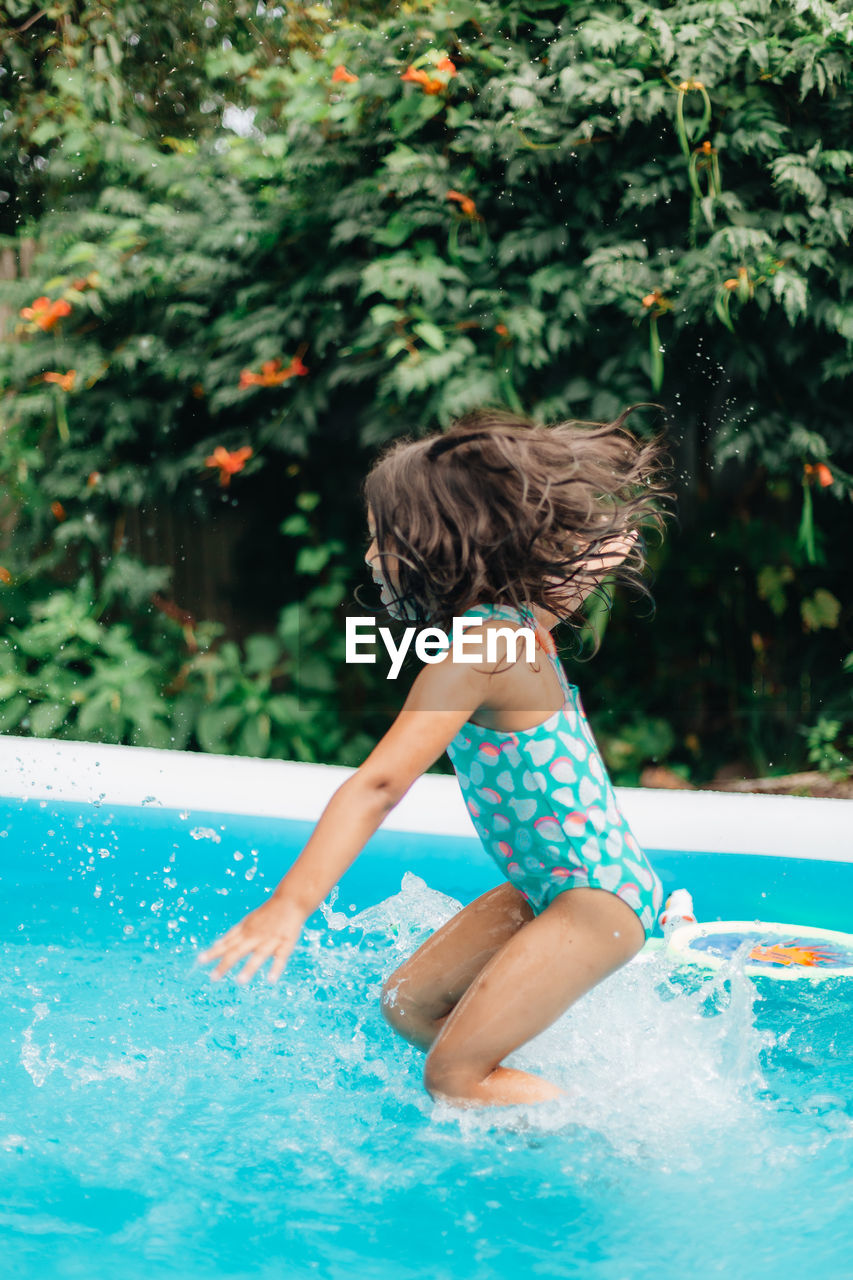 Diverse mixed race toddler girl at home having fun in kiddie pool in backyard being very happy