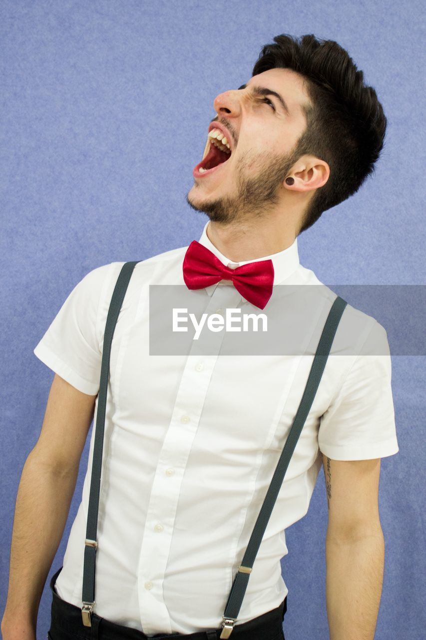 Young man screaming while standing against wall