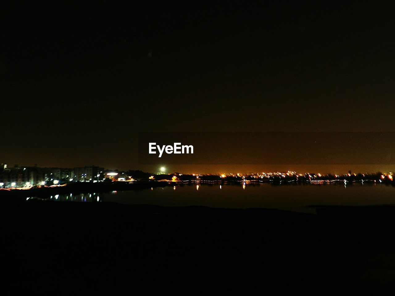 Scenic view of river by illuminated city against clear sky at night