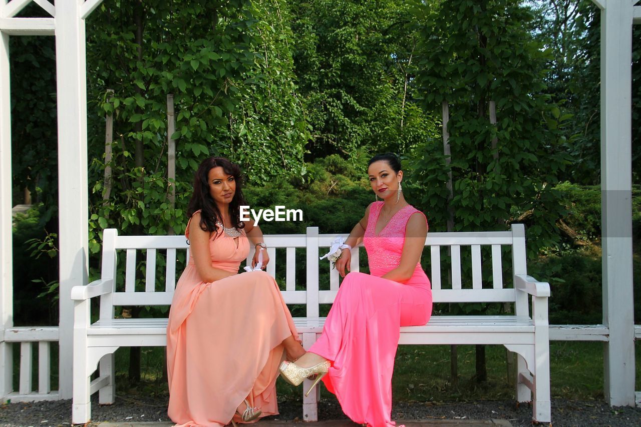 Portrait of beautiful women in wedding dresses sitting on bench in garden