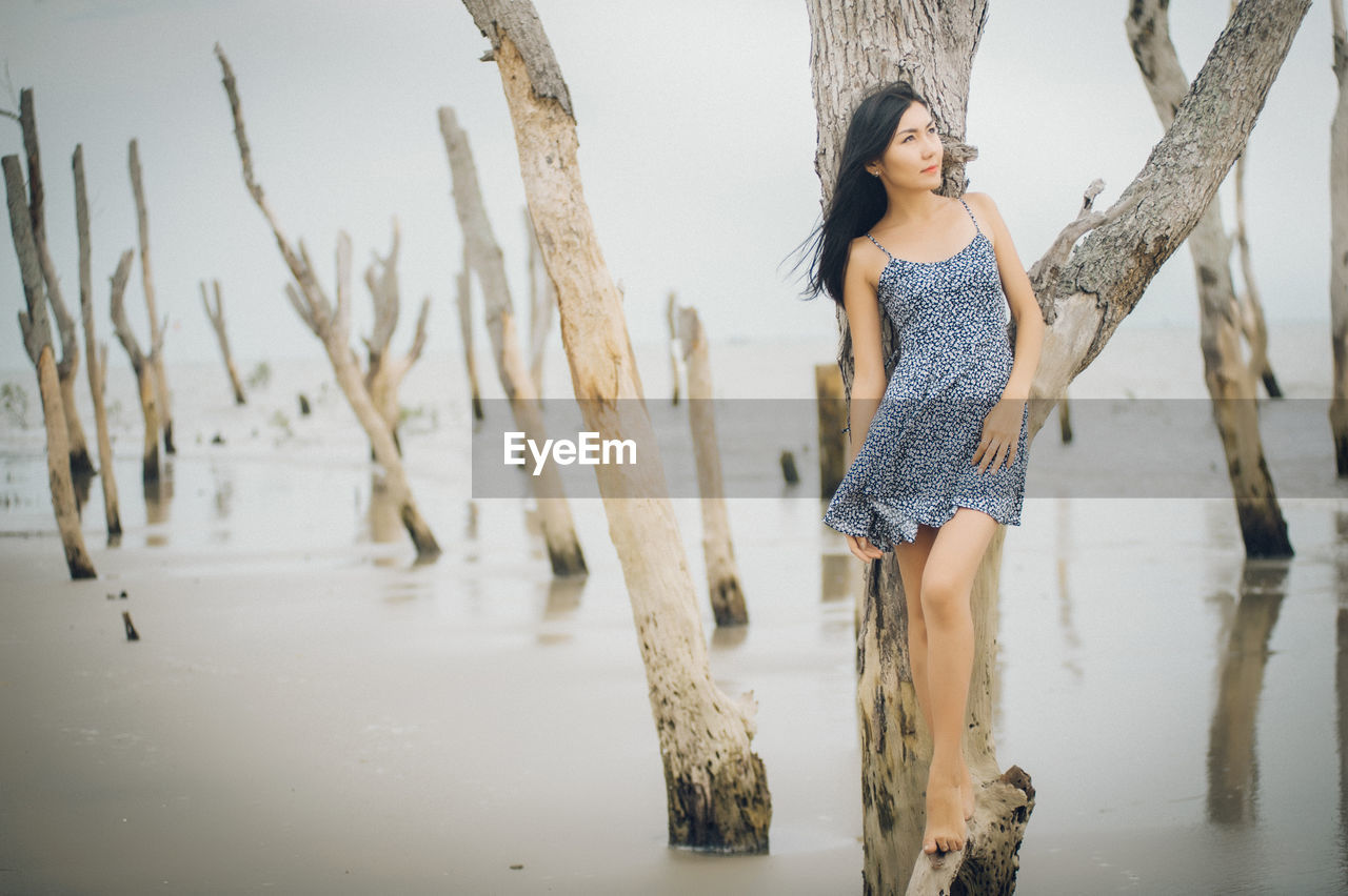 Full length of young woman standing on dead tree in lake