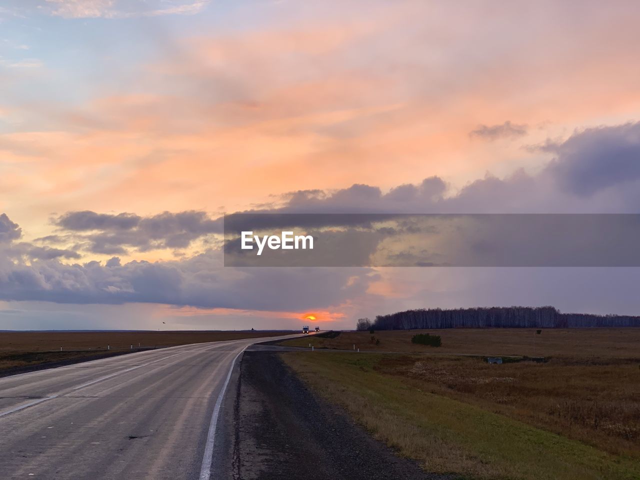 ROAD PASSING THROUGH FIELD AGAINST SKY DURING SUNSET