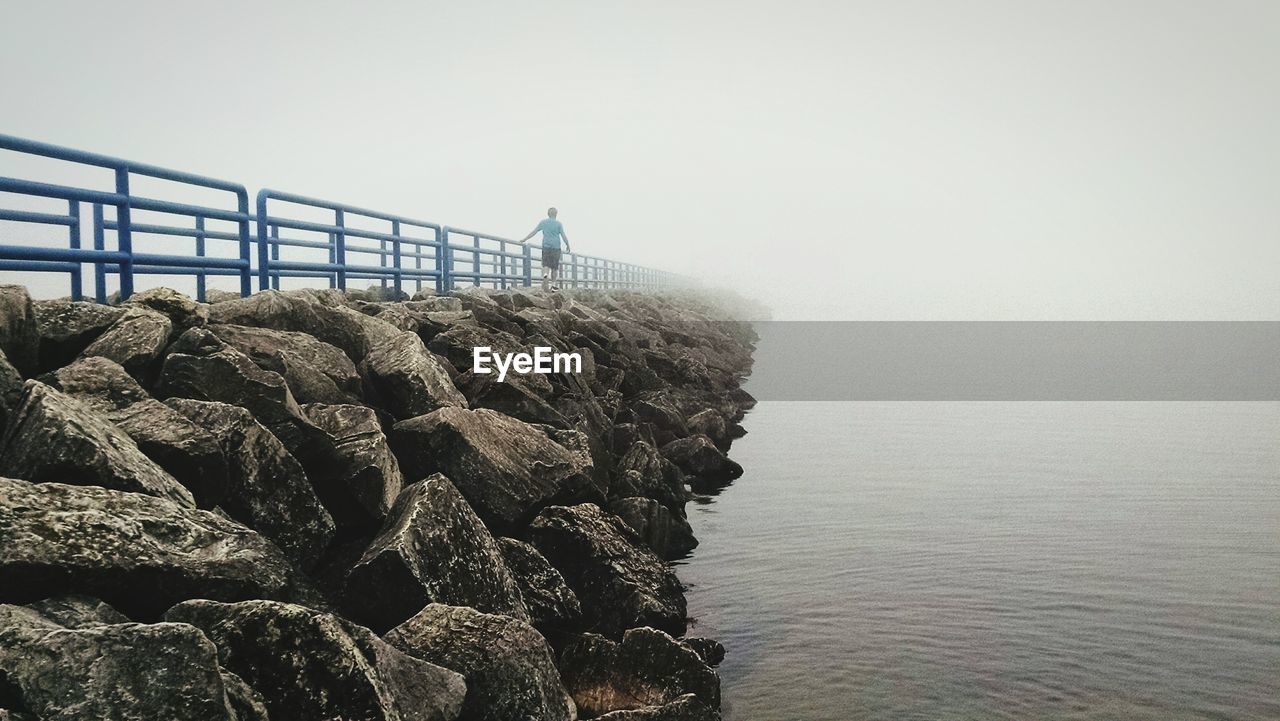 Boy walking on pier at lake in foggy weather