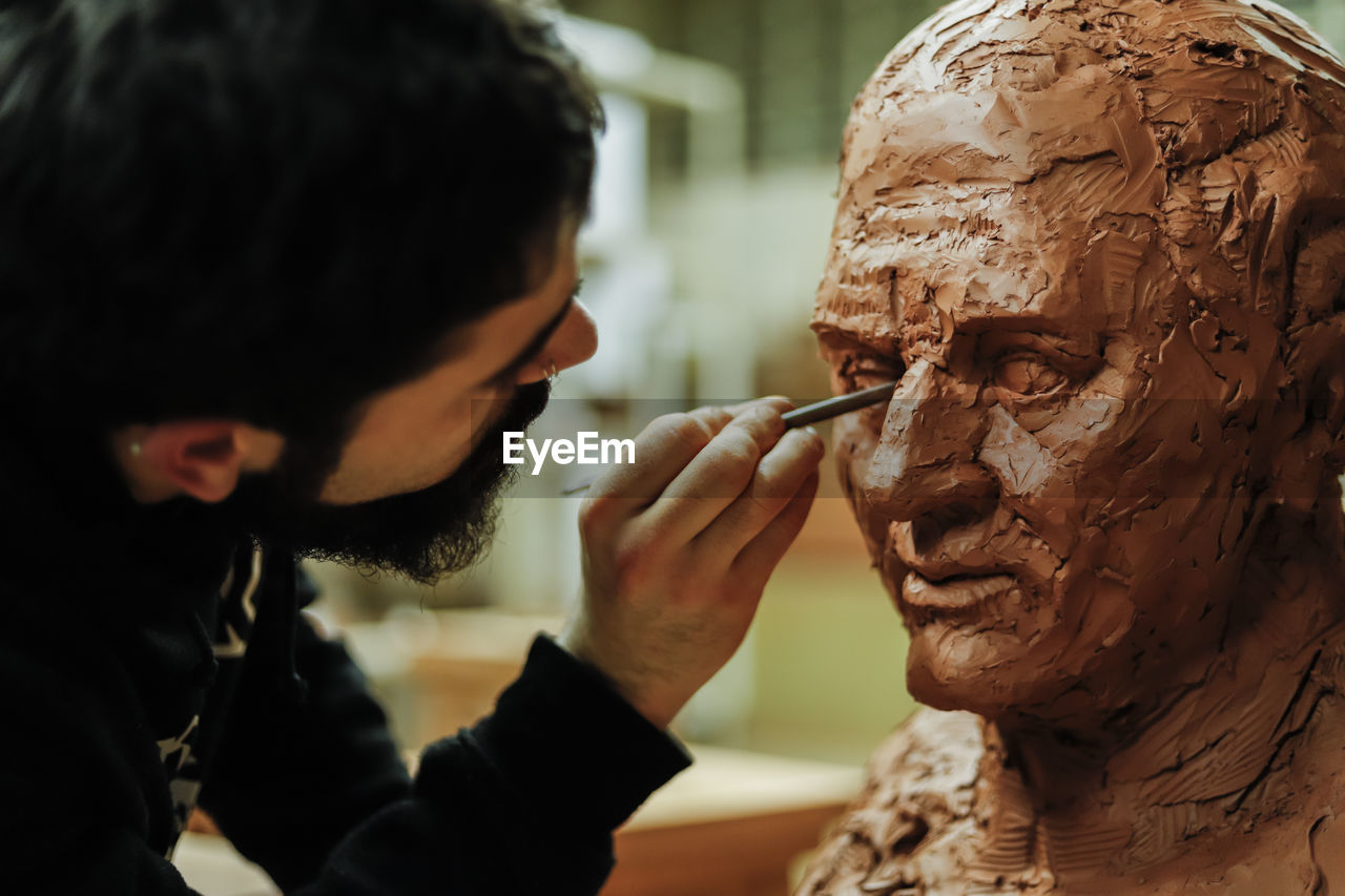 Focused sculptor finishing a clay head in an art studio