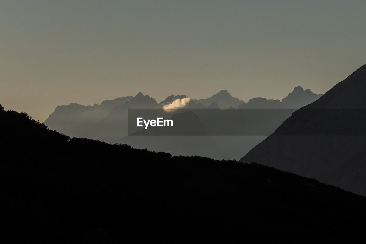 mountain, sky, scenics - nature, landscape, environment, mountain range, beauty in nature, silhouette, dawn, nature, horizon, tranquility, travel, land, no people, morning, tranquil scene, travel destinations, sunrise, darkness, mountain peak, outdoors, summit, cloud, copy space, tourism, non-urban scene, panoramic, ridge, idyllic