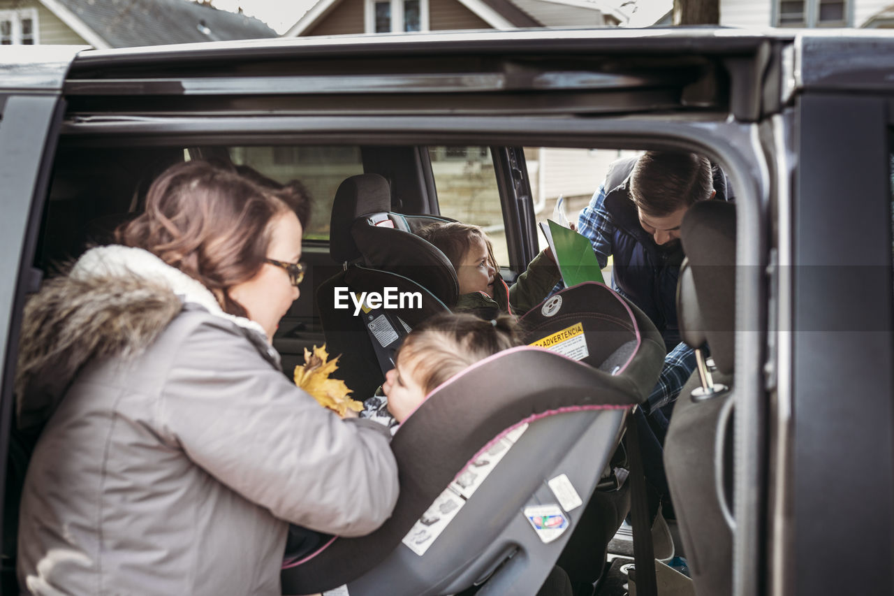 Parents adjusting girls on car seats