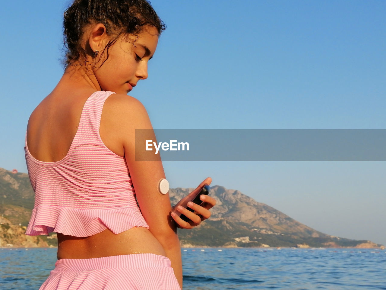  girl reads glucose level  from the white sensor on arm with cgm device before enters the sea. 