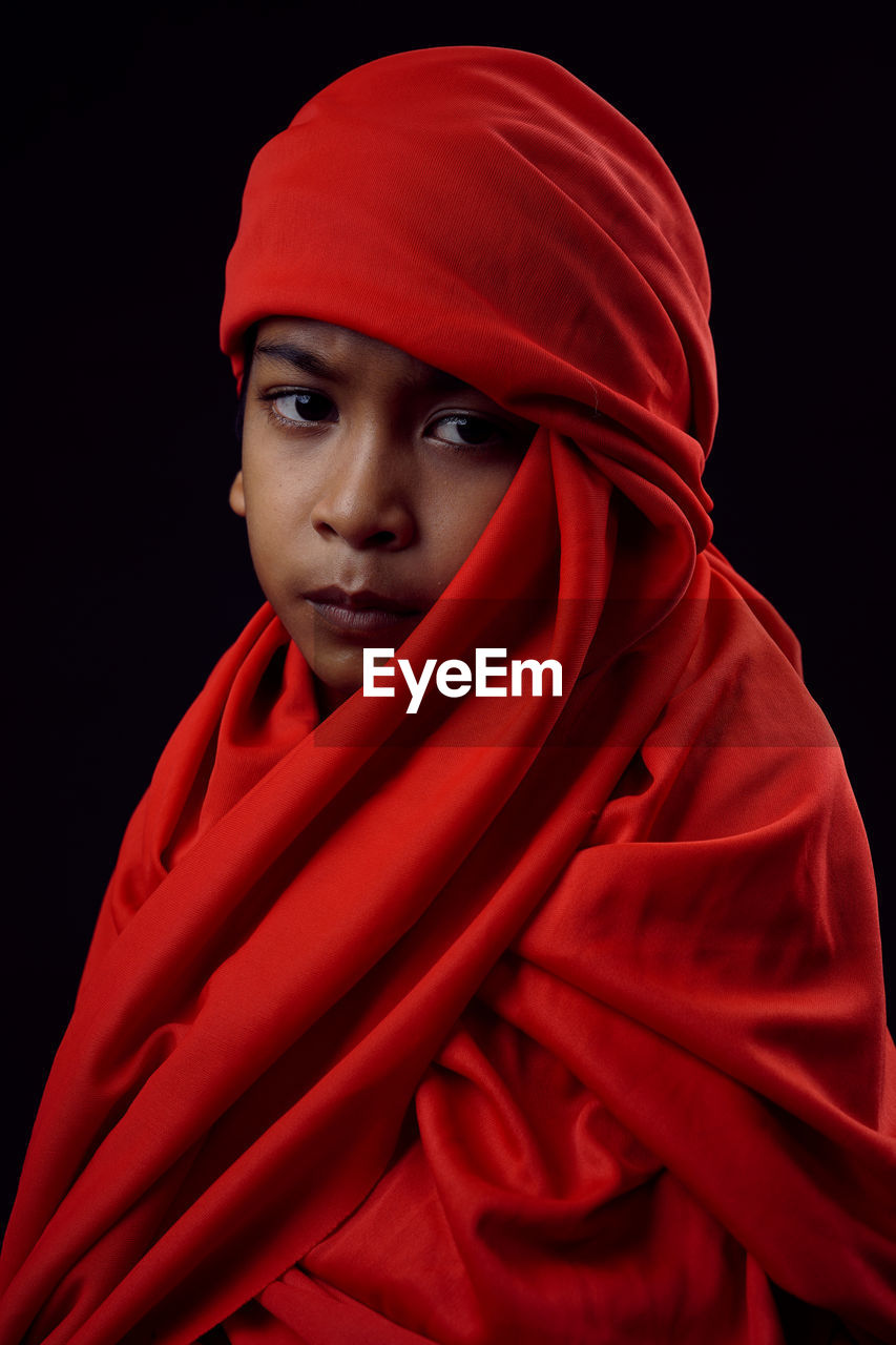 Portrait of boy wearing red textile against black background