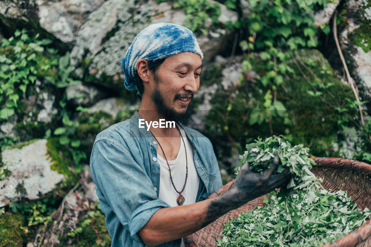 Smiling man holding basket with plants while standing against rocks