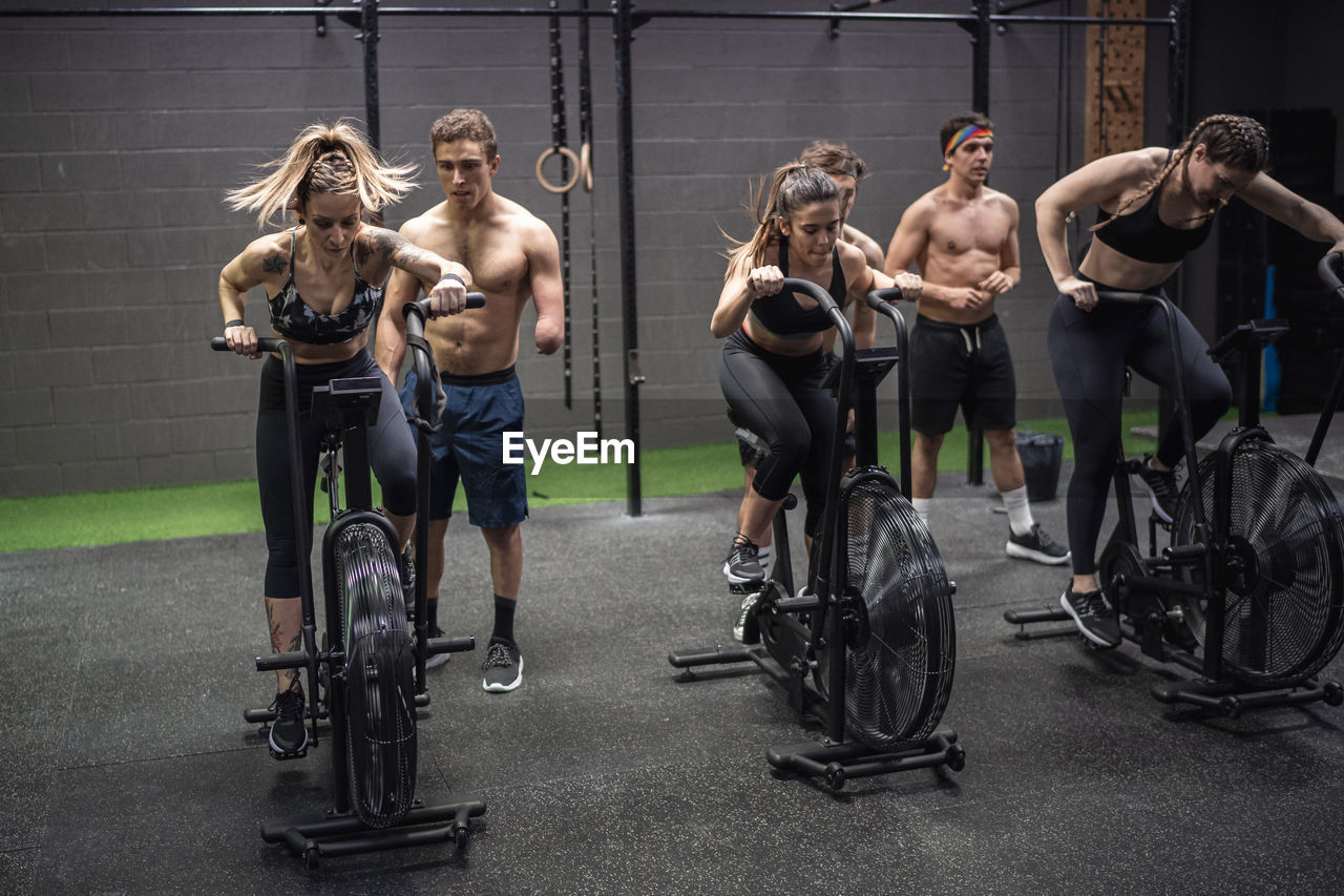 Men motivating women exercising on fitness bike at gym