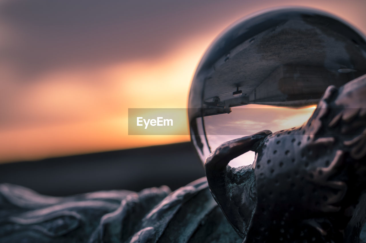 CLOSE-UP OF MAN HOLDING CAMERA AGAINST SEA DURING SUNSET