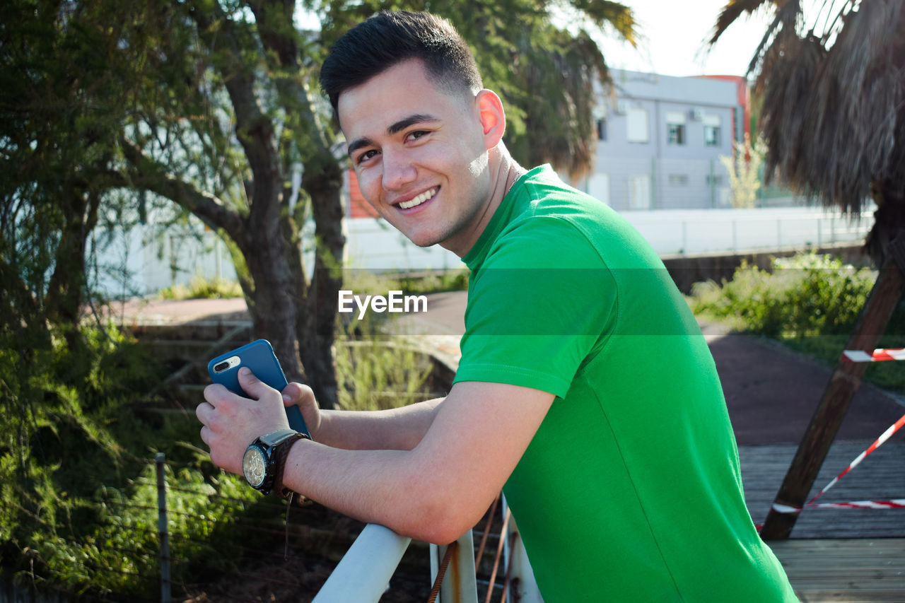 Side view portrait of young man smiling while leaning on railing