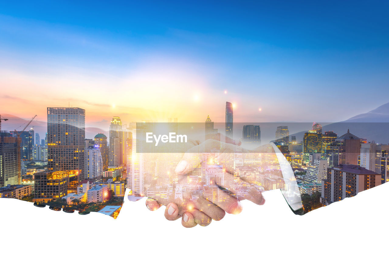 DIGITAL COMPOSITE IMAGE OF HAND HOLDING CITYSCAPE DURING SUNSET