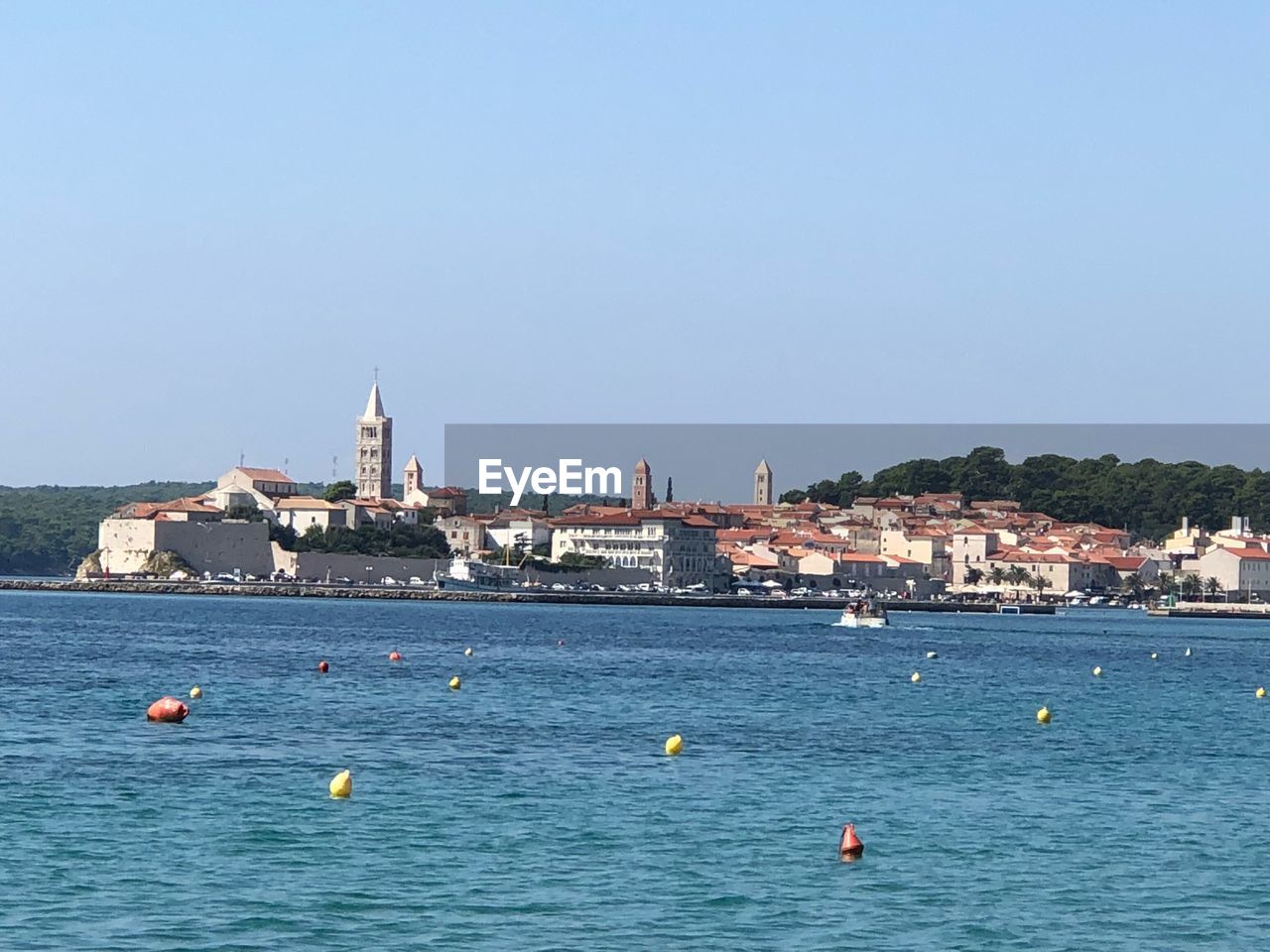 Sailboats in sea by buildings against clear blue sky