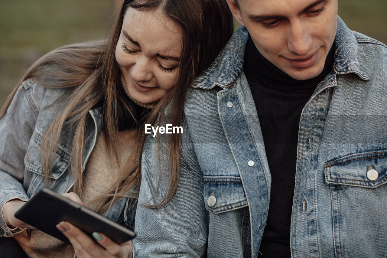 A young fashionable couple smiles while looking at the phone in the park