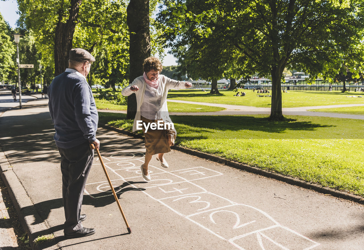 Senior woman playing hopscotch while husband watching her