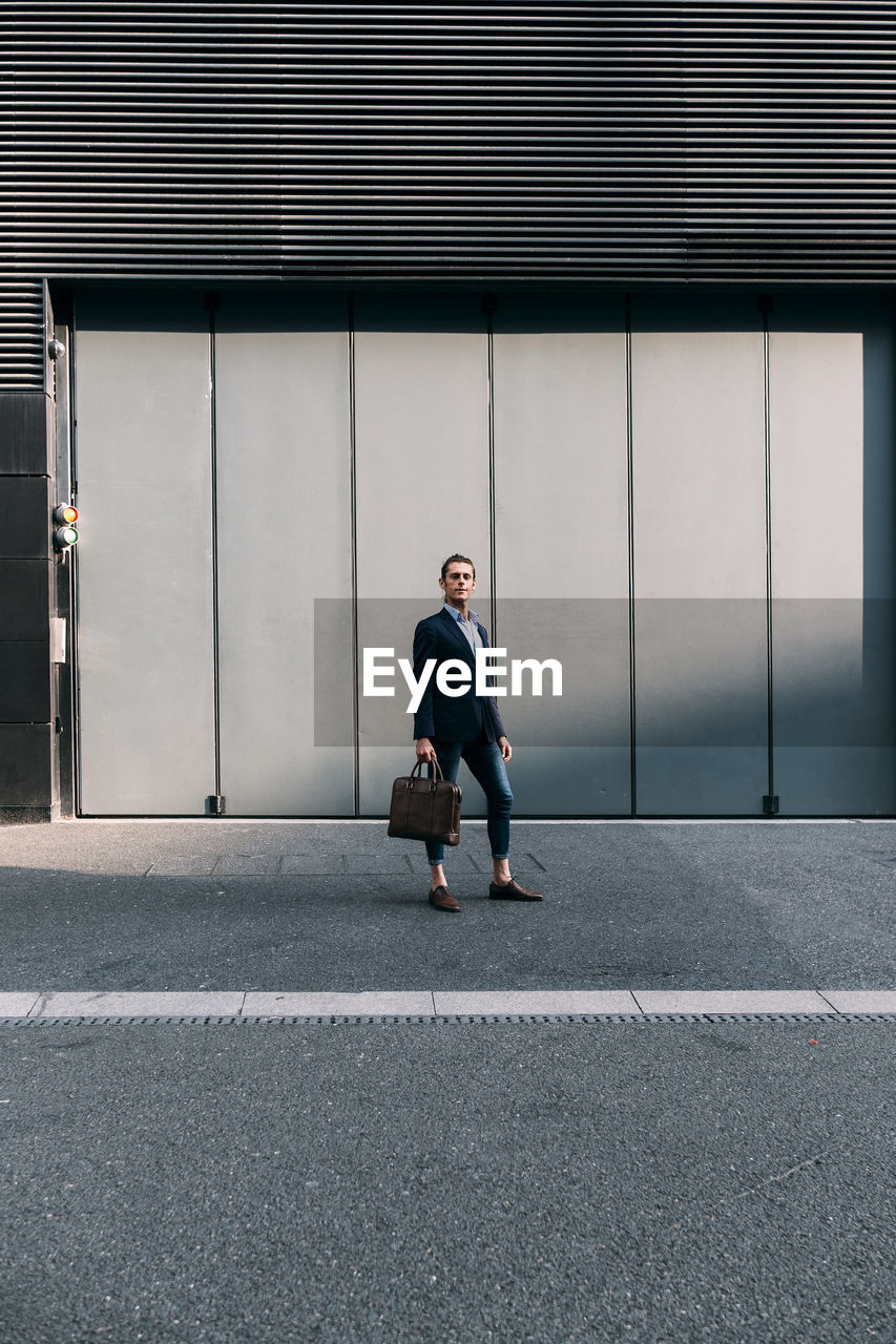 Businessman holding briefcase while standing on footpath