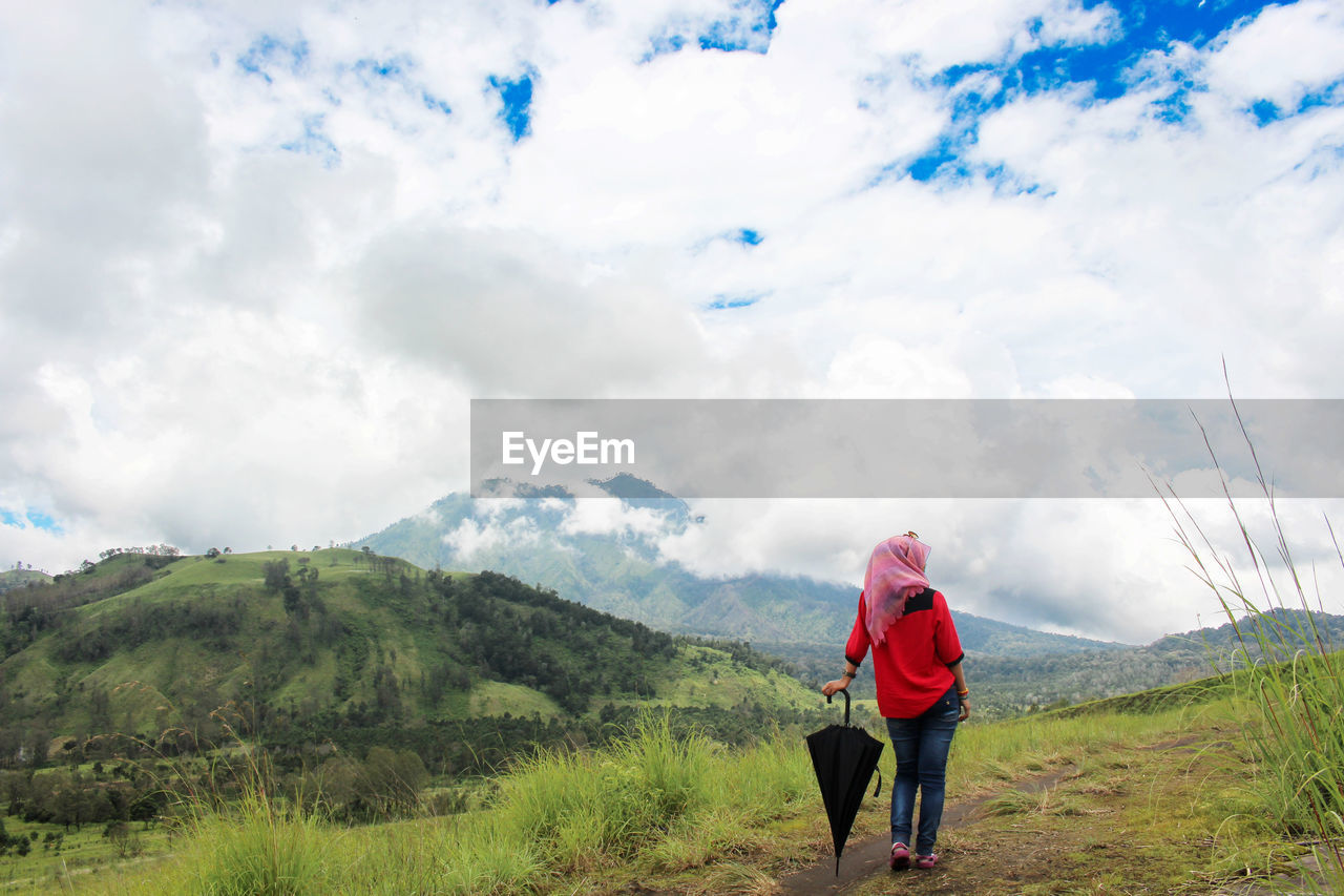 Rear view of woman standing on land against cloudy sky