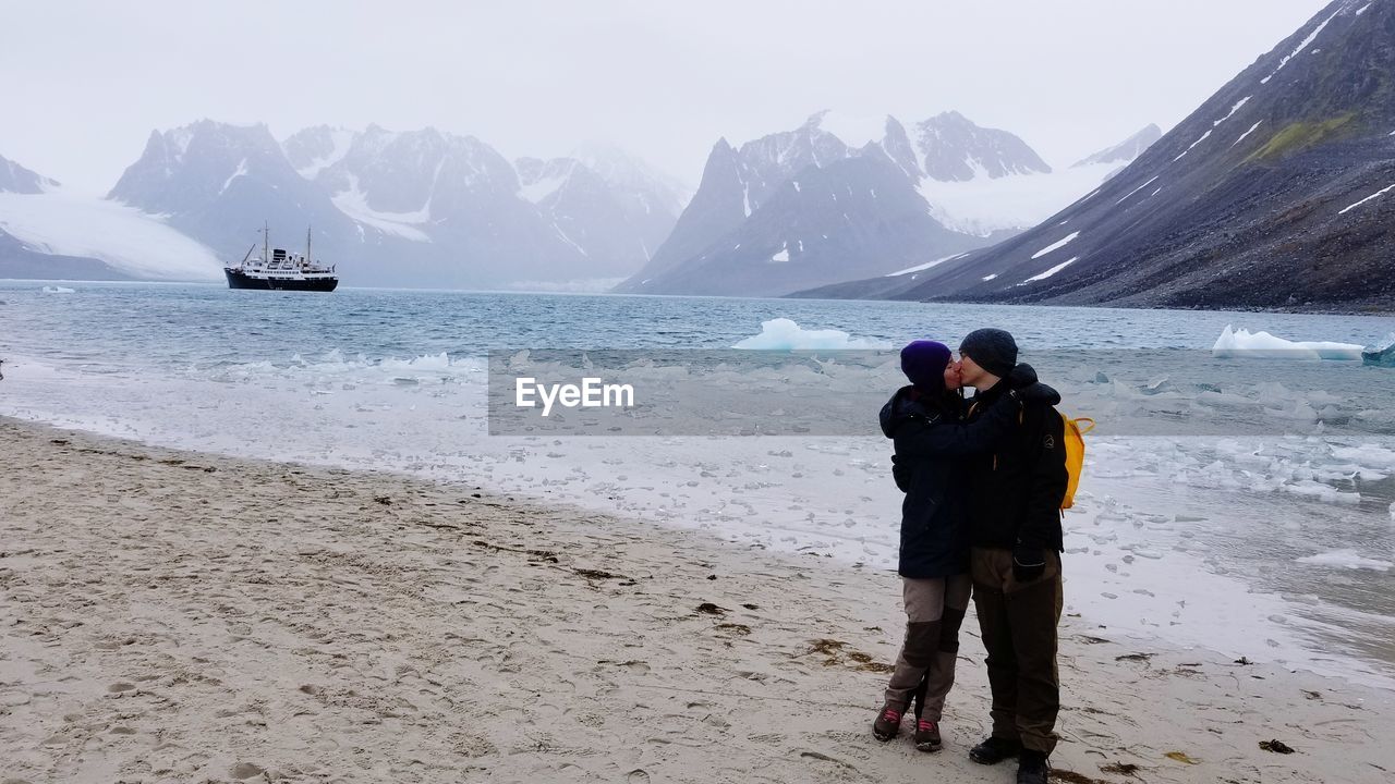 Full length of couple kissing while standing by frozen lake during winter
