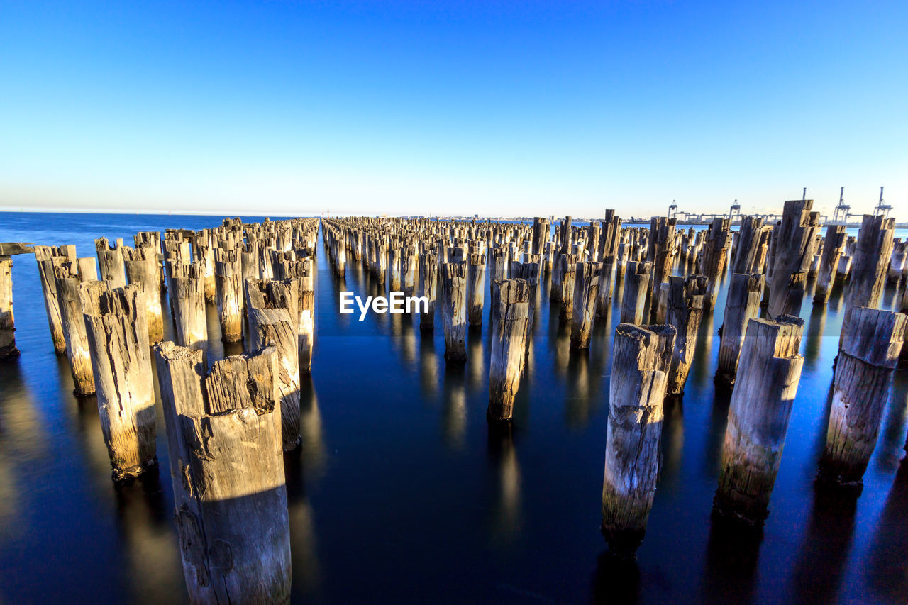 Panoramic view of wooden posts at princes pier in sea against clear blue sky