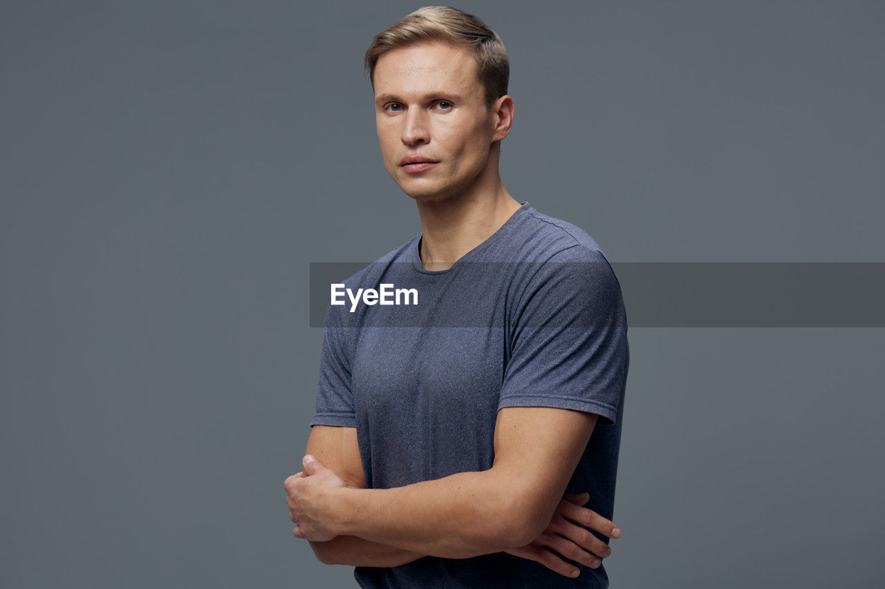 studio shot, one person, portrait, gray, gray background, indoors, looking at camera, adult, young adult, sleeve, standing, casual clothing, t-shirt, front view, men, arms crossed, copy space, arm, waist up, colored background, photo shoot, serious, looking, strength, individuality