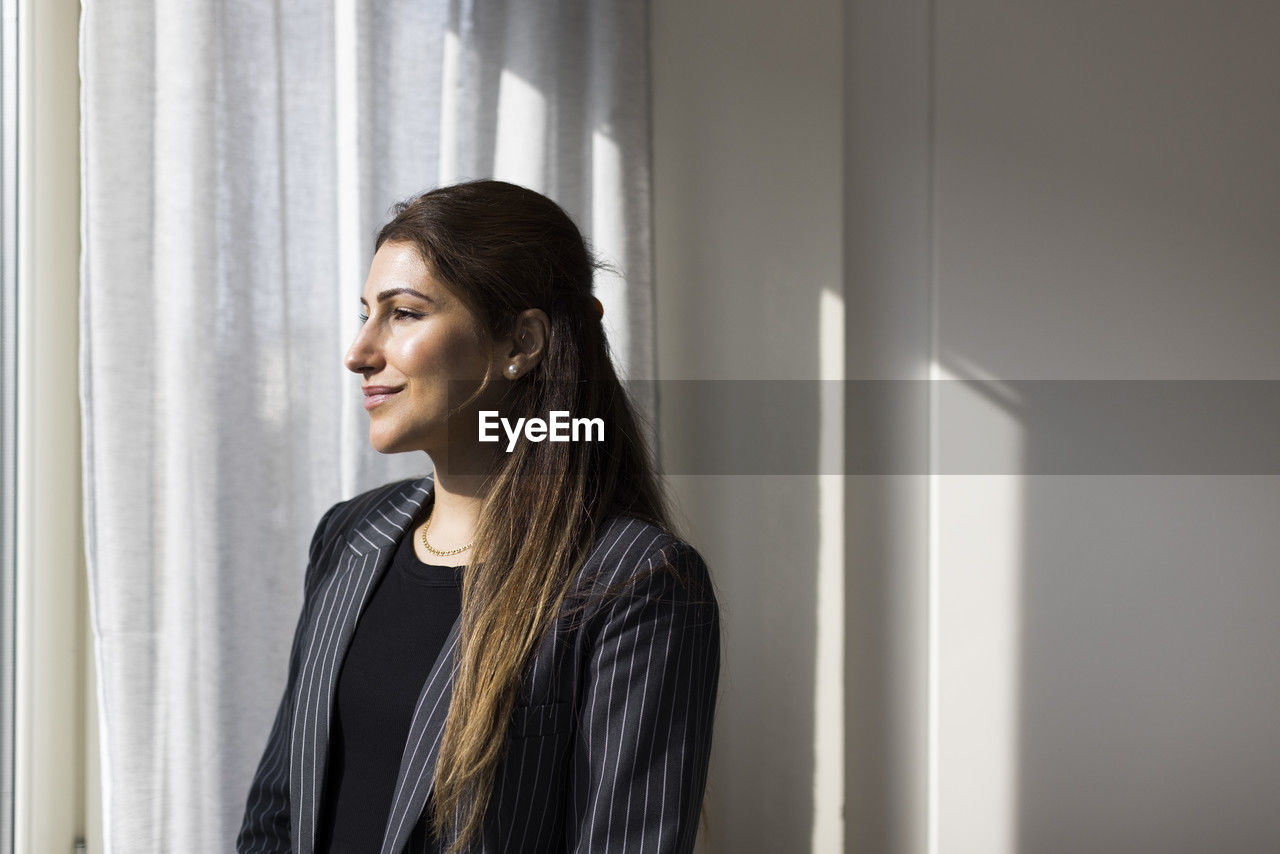 Smiling female real estate agent looking through window at new home