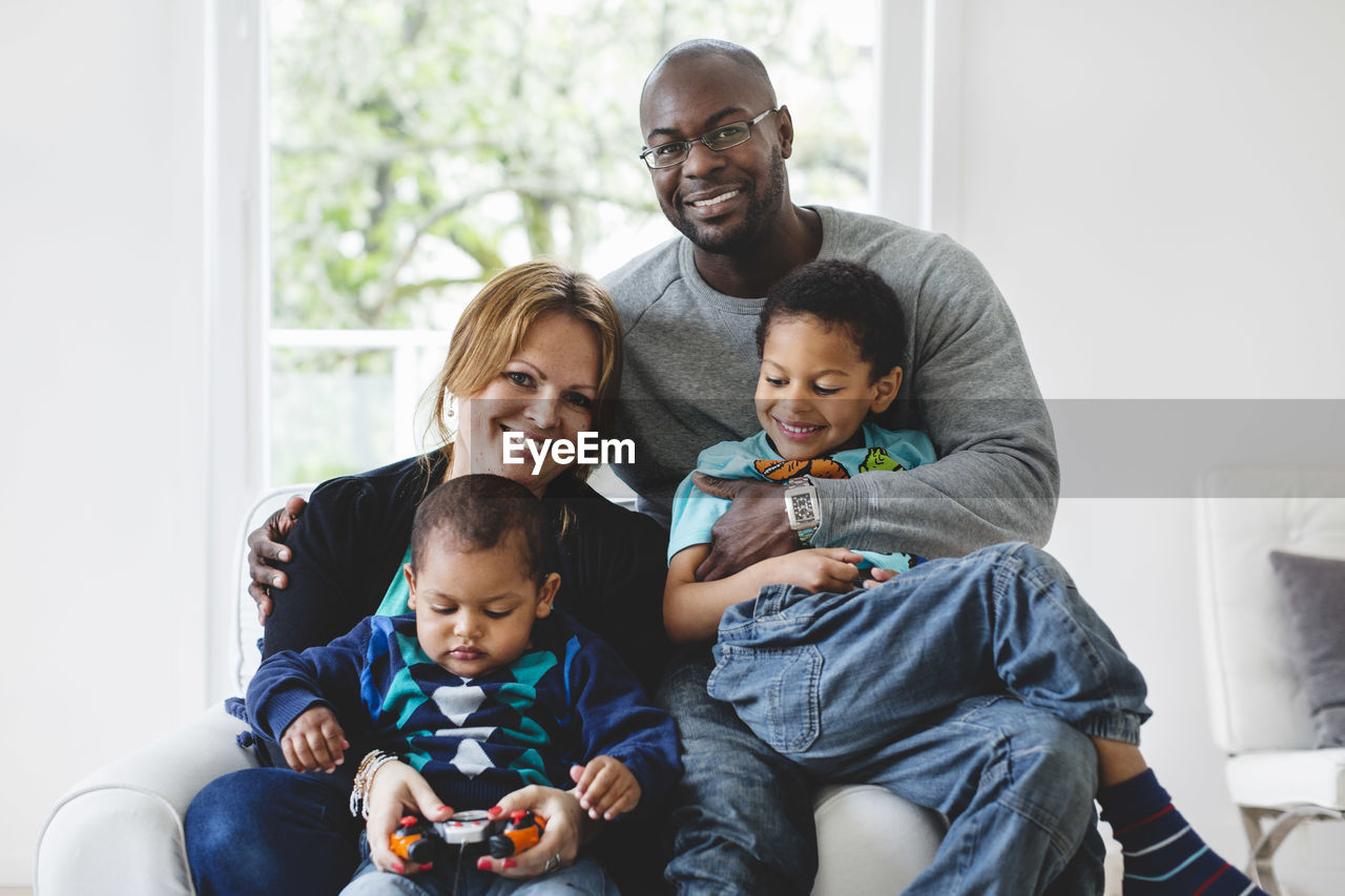 Portrait of happy multi-ethnic parents sitting with children at home