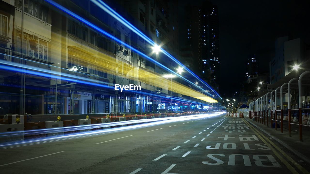 Light trails on road by buildings at night