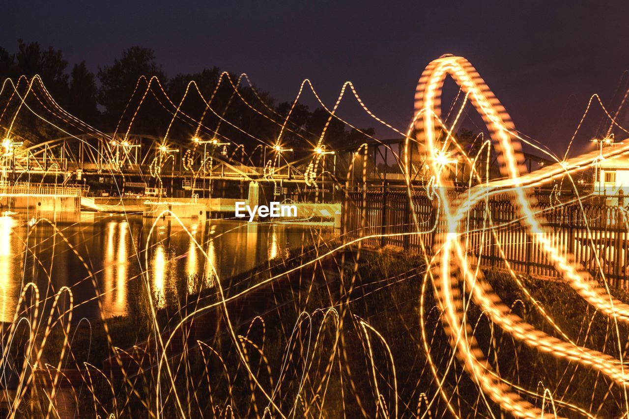 ILLUMINATED BRIDGE OVER RIVER AGAINST SKY AT NIGHT