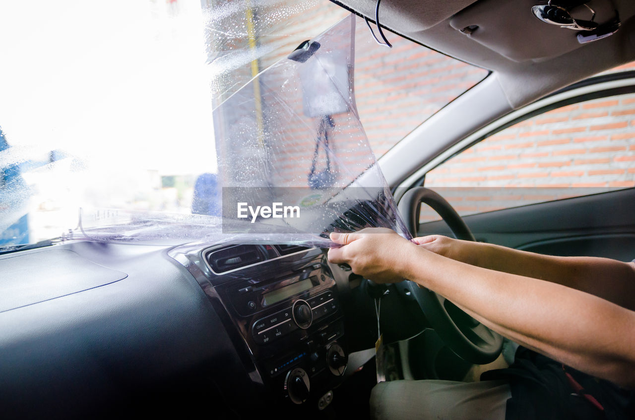 Cropped hands of woman removing plastic from car windshield