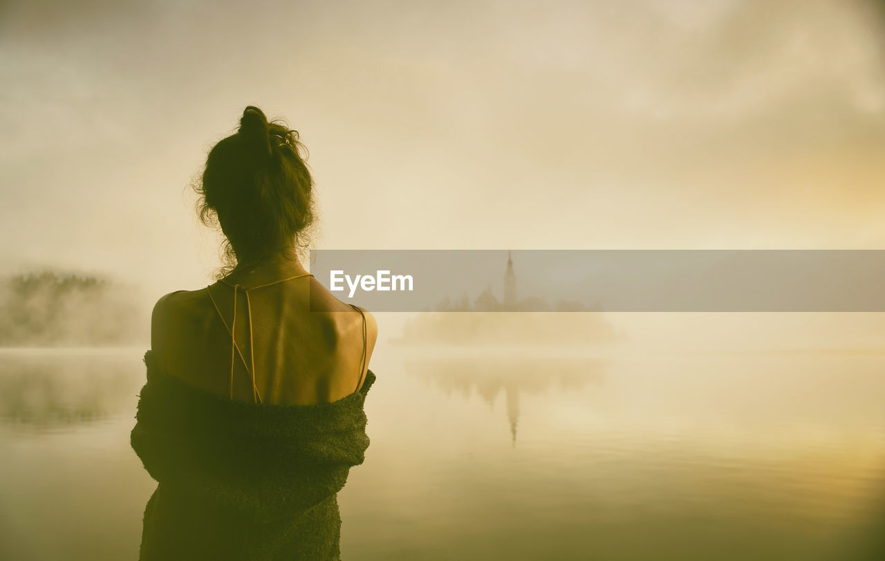 Woman in gray coat watching a sunrise among the fog on the shores of lake bled, slovenia v