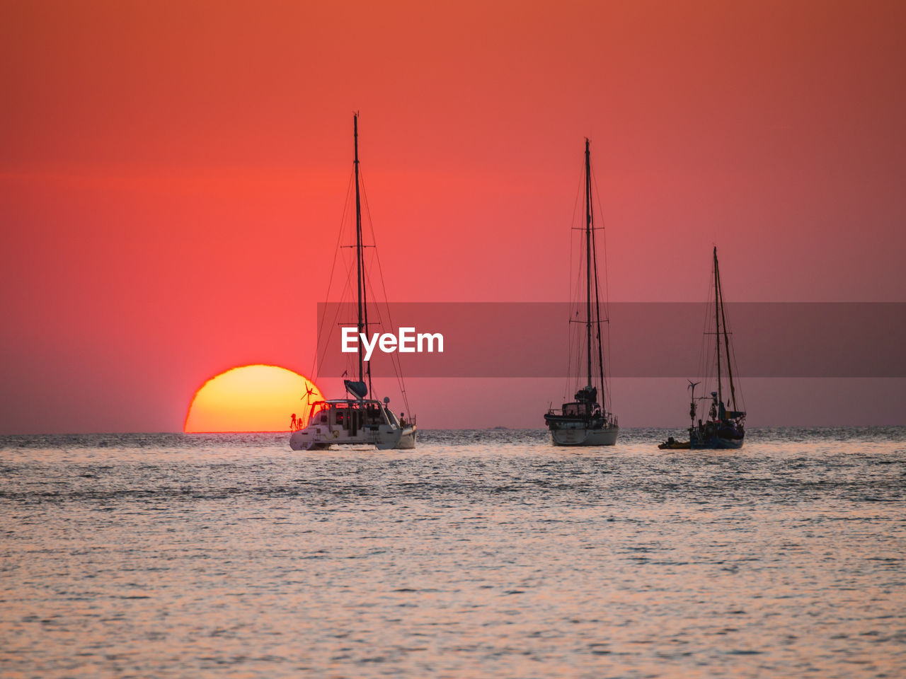 Sailboat sailing on sea against orange sky