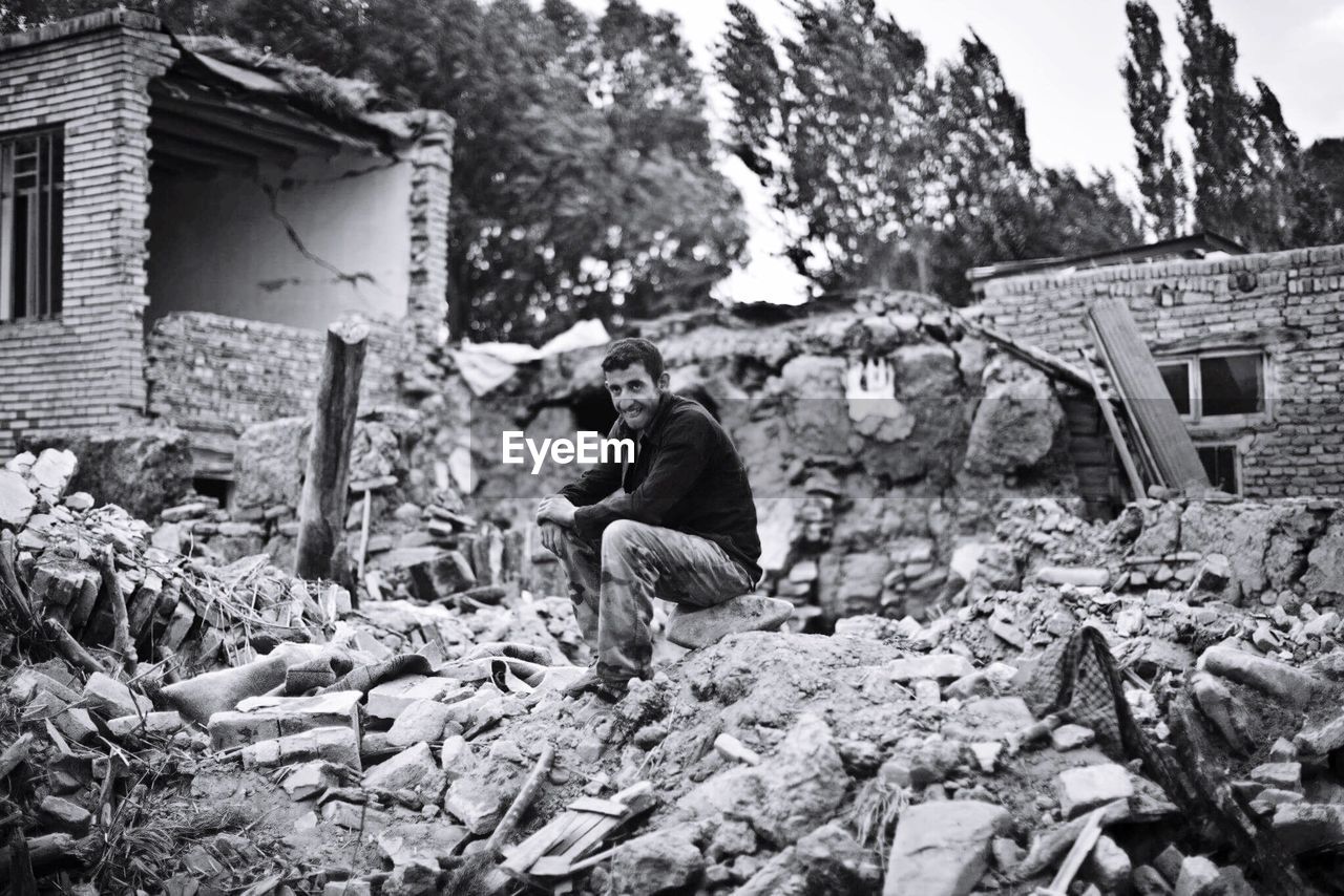 Man sitting on rock amidst demolished building