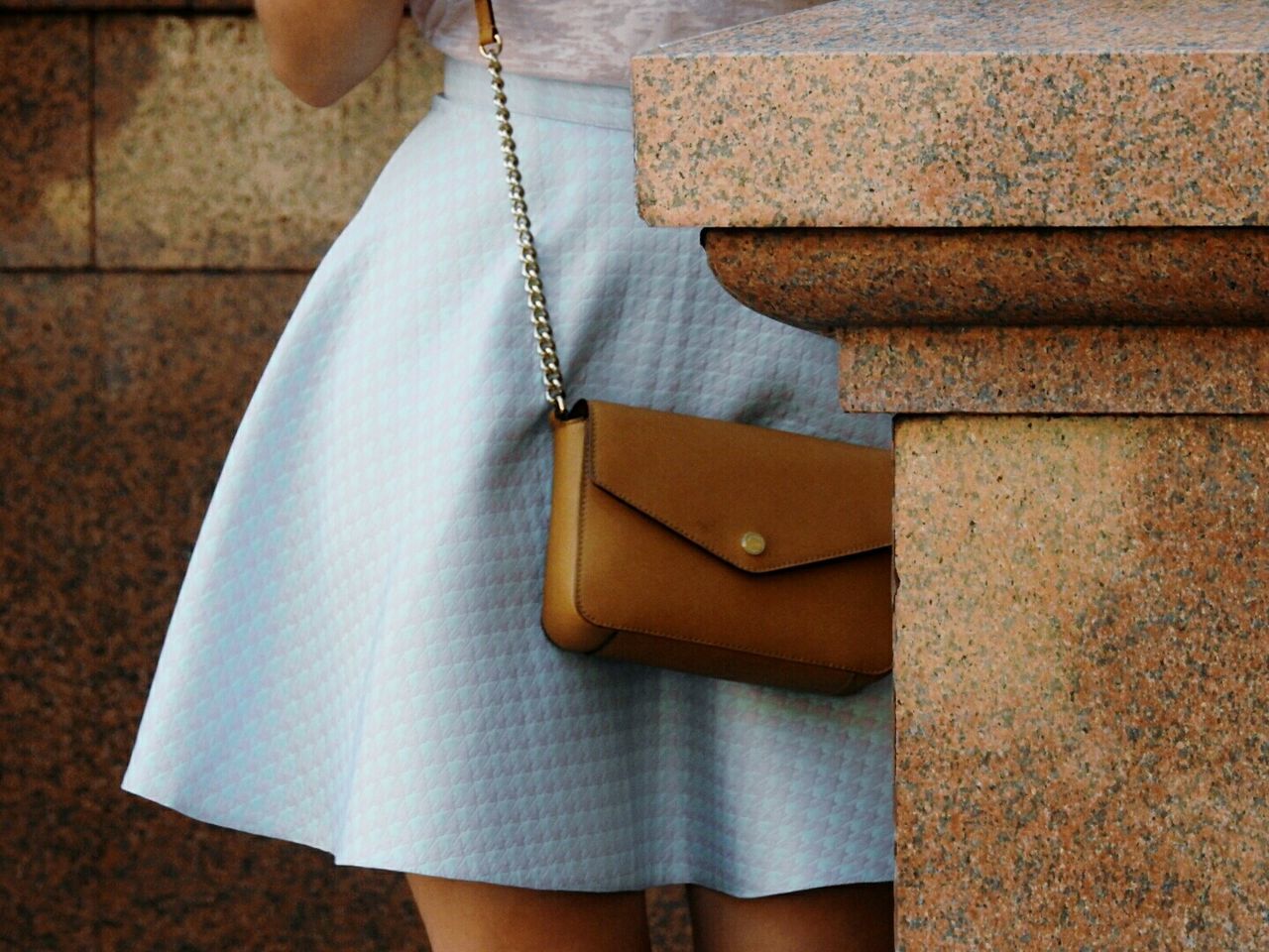 Midsection of woman with sling bag standing by marble wall