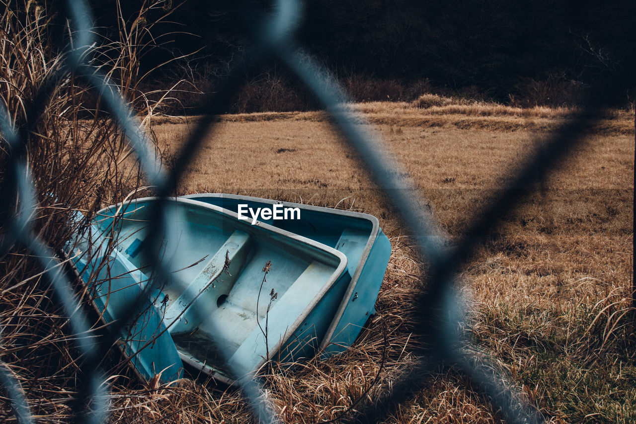 View of abandoned boat on field seen through chainlink fence