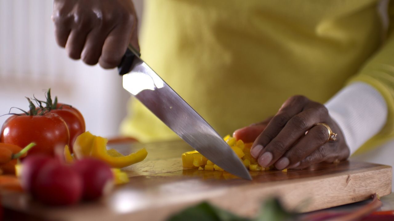 Midsection of person chopping vegetable on cutting board in kitchen
