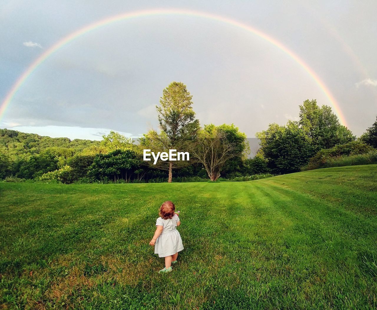 Full length of girl standing on field against rainbow in sky