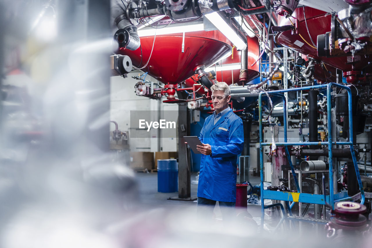 Male engineer working on digital tablet while standing against machinery equipment in factory