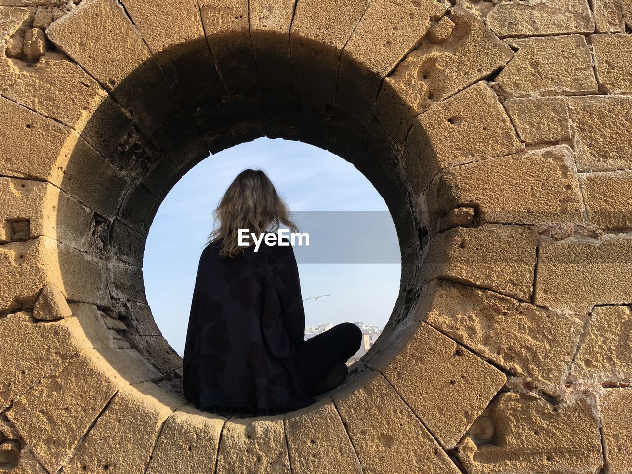 Rear view of woman sitting amidst stone wall